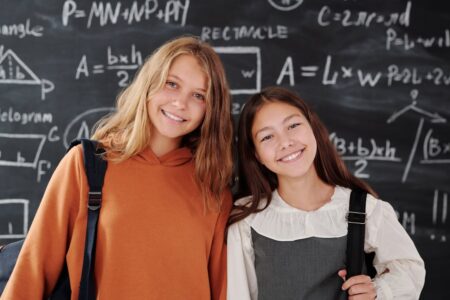 dwie dziewczynki stojące przy tablicy zapisanej we wzory matematyczne